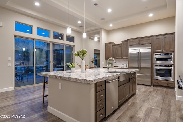 kitchen with sink, wood-type flooring, decorative light fixtures, appliances with stainless steel finishes, and an island with sink