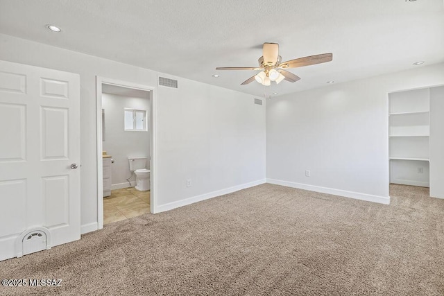 unfurnished bedroom featuring connected bathroom, a closet, light colored carpet, ceiling fan, and a walk in closet