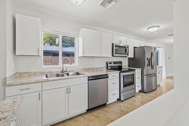 kitchen with light stone countertops, stainless steel appliances, light tile patterned floors, white cabinets, and sink