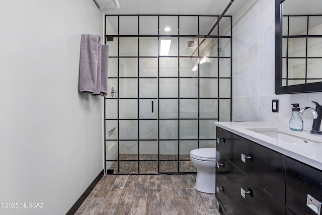 bathroom with tile walls, toilet, vanity, and a tile shower