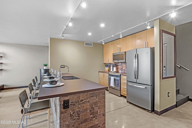 kitchen with rail lighting, appliances with stainless steel finishes, light brown cabinets, a kitchen breakfast bar, and sink