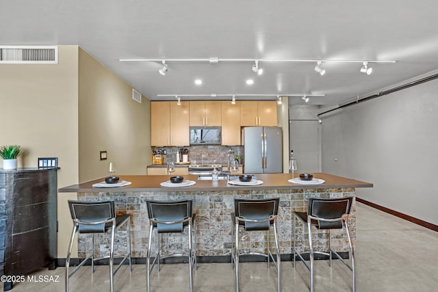 kitchen with backsplash, sink, a kitchen breakfast bar, light brown cabinetry, and stainless steel fridge