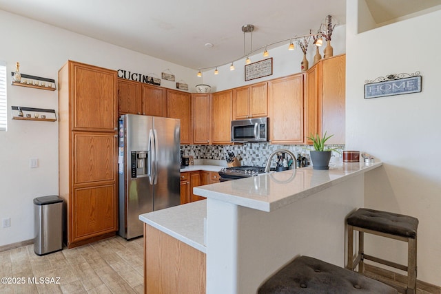 kitchen featuring appliances with stainless steel finishes, decorative light fixtures, tasteful backsplash, light hardwood / wood-style floors, and kitchen peninsula