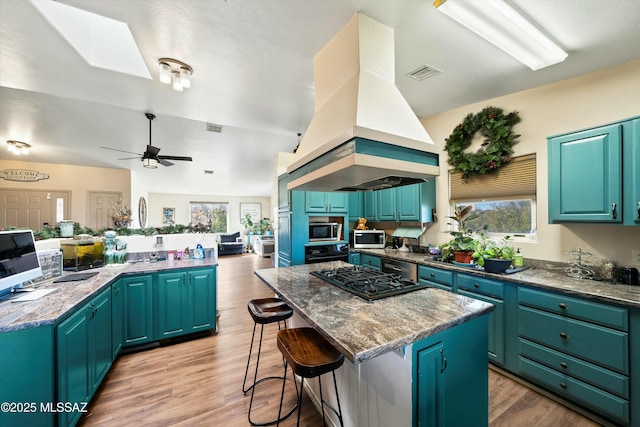 kitchen featuring oven, ceiling fan, island exhaust hood, gas stovetop, and a kitchen island