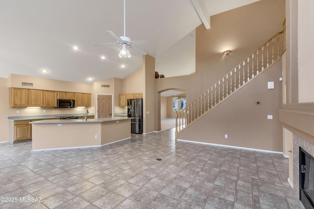 kitchen featuring stainless steel appliances, an island with sink, a tile fireplace, and light brown cabinets