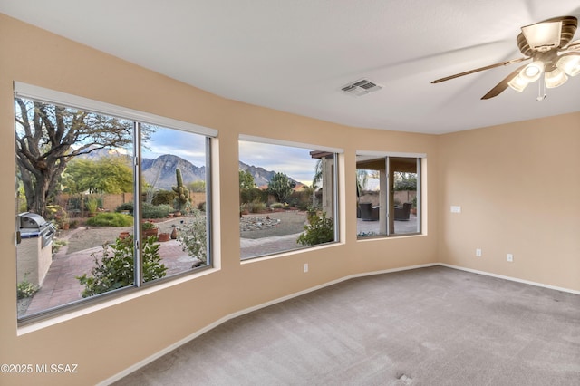 unfurnished room with ceiling fan, a healthy amount of sunlight, carpet flooring, and a mountain view