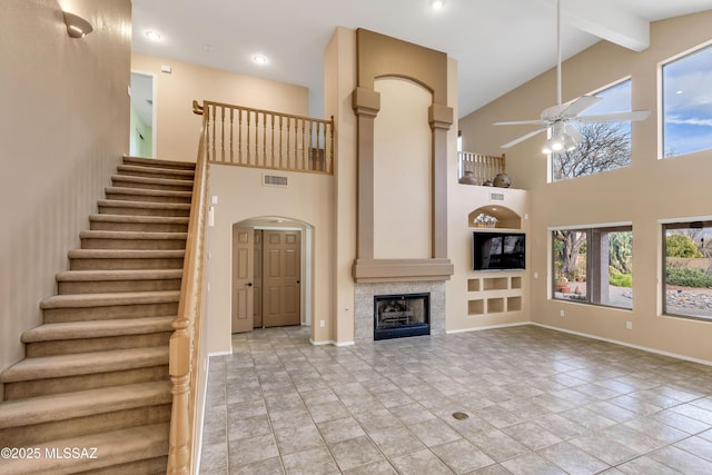 unfurnished living room featuring beamed ceiling, high vaulted ceiling, a fireplace, and ceiling fan