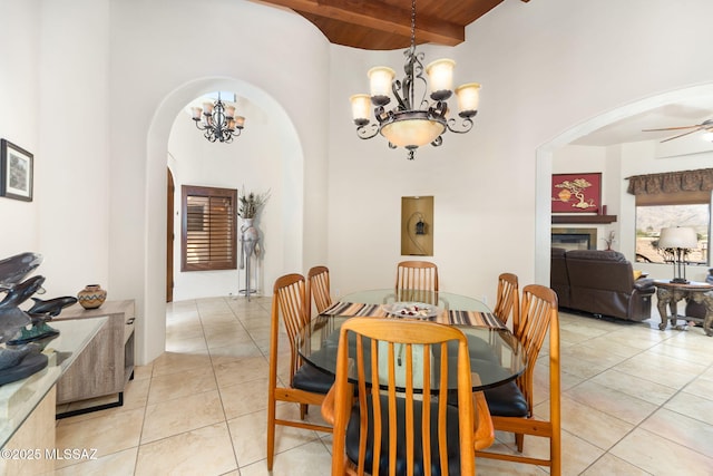 dining space featuring ceiling fan with notable chandelier, a high ceiling, wood ceiling, light tile patterned flooring, and beam ceiling