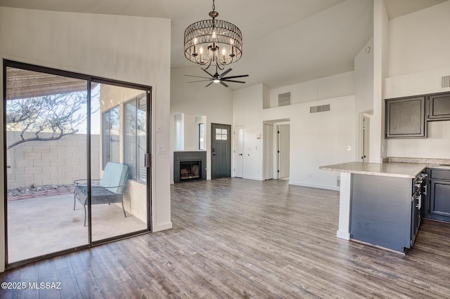 kitchen featuring decorative light fixtures, kitchen peninsula, ceiling fan with notable chandelier, dark hardwood / wood-style floors, and high vaulted ceiling