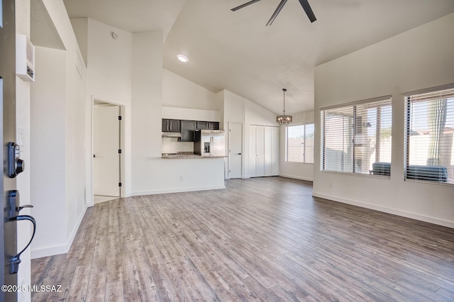 unfurnished living room with ceiling fan with notable chandelier, high vaulted ceiling, and dark hardwood / wood-style floors