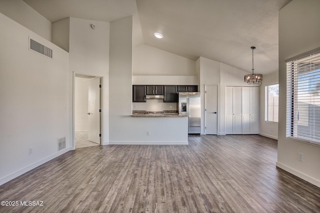 unfurnished living room with dark hardwood / wood-style flooring, an inviting chandelier, and high vaulted ceiling