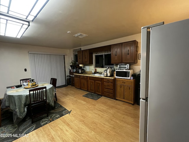 kitchen with sink, stainless steel fridge, light wood-type flooring, and dark brown cabinetry