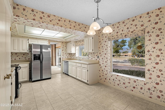 kitchen featuring a textured ceiling, stainless steel appliances, sink, hanging light fixtures, and a raised ceiling