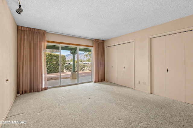 unfurnished bedroom with a textured ceiling, carpet flooring, two closets, and access to outside