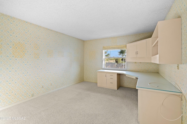 unfurnished office featuring a textured ceiling, light carpet, and built in desk