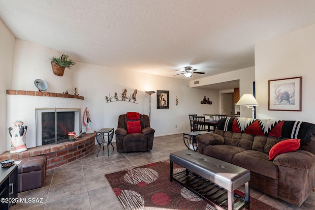 tiled living room with a brick fireplace, a textured ceiling, and ceiling fan