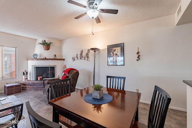 dining room featuring a brick fireplace, a textured ceiling, ceiling fan, and tile patterned flooring