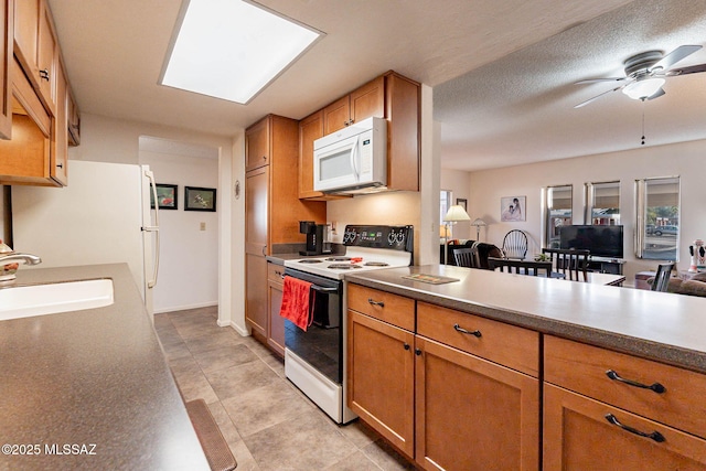 kitchen featuring a skylight, ceiling fan, white appliances, a textured ceiling, and sink