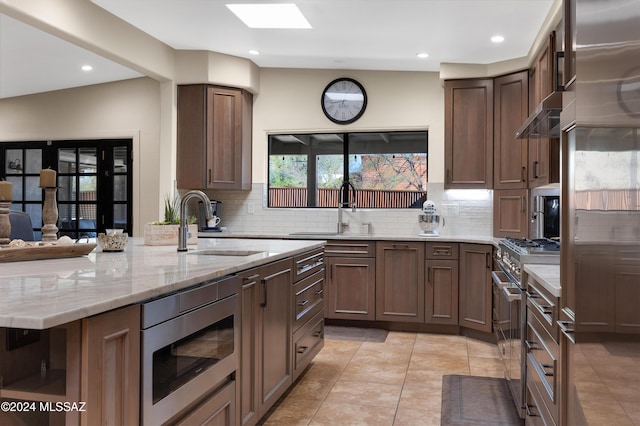 kitchen featuring light stone countertops, stainless steel appliances, tasteful backsplash, and sink