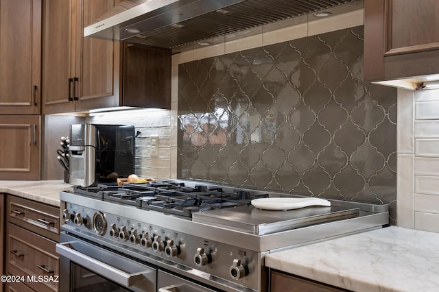 kitchen featuring light stone counters, wall chimney exhaust hood, and high end stove