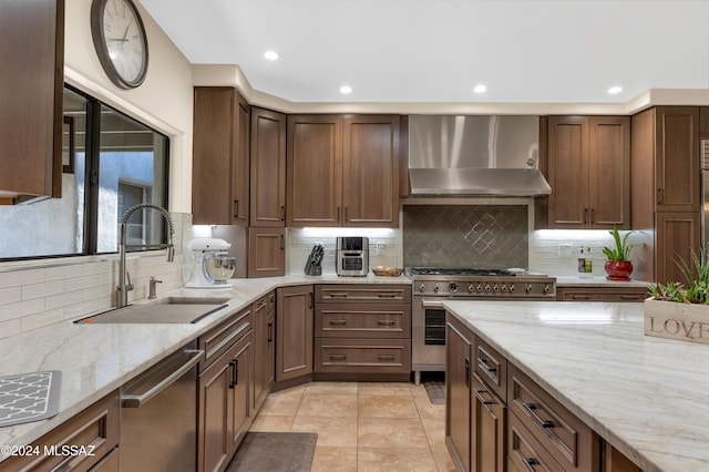 kitchen with stainless steel appliances, backsplash, wall chimney exhaust hood, light stone counters, and sink