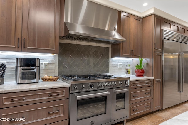 kitchen with decorative backsplash, light tile patterned flooring, light stone countertops, wall chimney exhaust hood, and high quality appliances