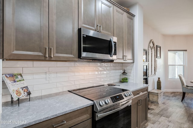 kitchen with stainless steel appliances, light hardwood / wood-style floors, backsplash, and light stone countertops