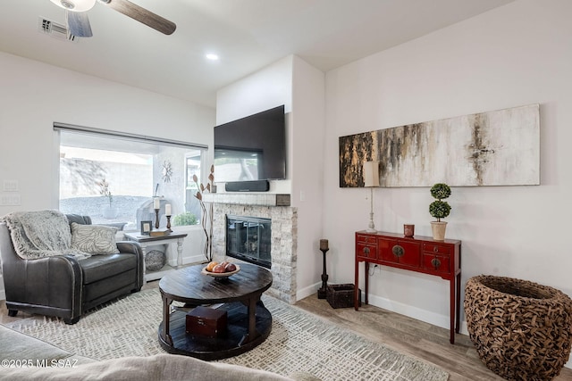 living room with ceiling fan, a stone fireplace, and hardwood / wood-style floors