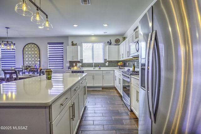 kitchen with stainless steel appliances, a center island, pendant lighting, white cabinets, and sink