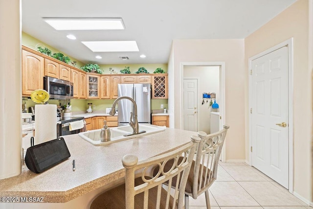 kitchen with a skylight, stainless steel appliances, a kitchen breakfast bar, sink, and light tile patterned flooring