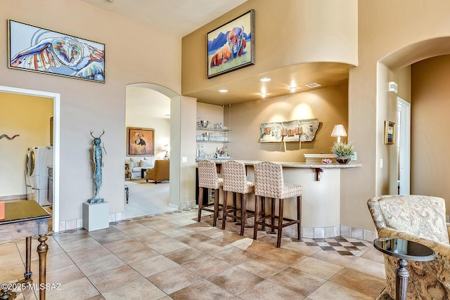 kitchen with light tile patterned floors, arched walkways, a breakfast bar area, a high ceiling, and light countertops