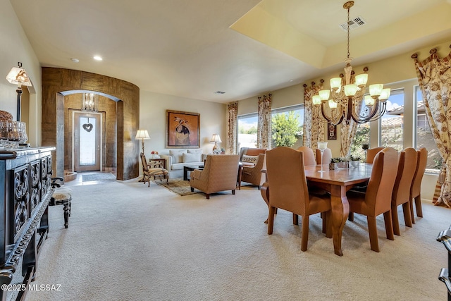 dining area featuring a chandelier, arched walkways, visible vents, and light colored carpet