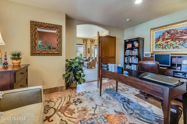 office area with arched walkways, light tile patterned flooring, and baseboards