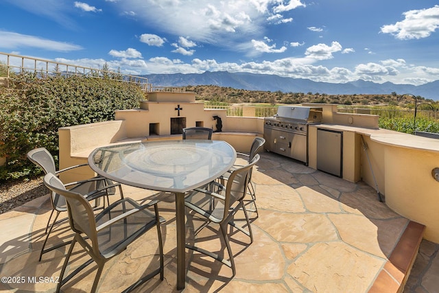 view of patio / terrace featuring outdoor dining area, area for grilling, an outdoor kitchen, a mountain view, and fence