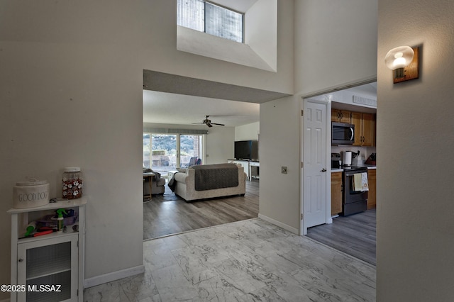 entryway featuring marble finish floor, a high ceiling, ceiling fan, and baseboards