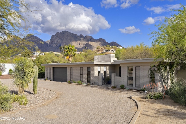 view of front of house featuring brick siding, an attached garage, a chimney, a mountain view, and driveway