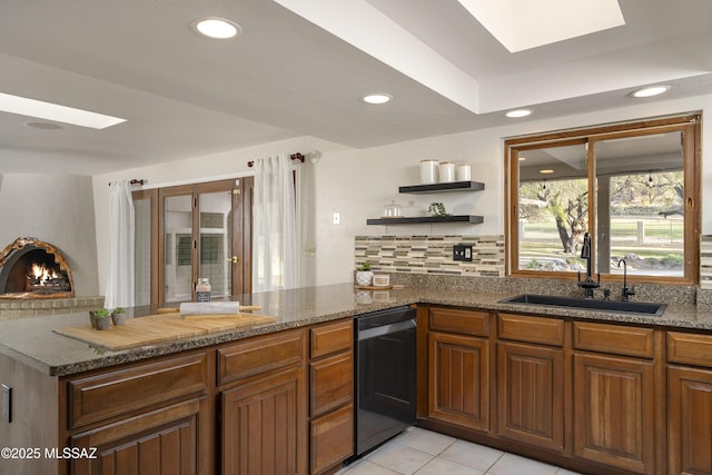 kitchen featuring dishwashing machine, a peninsula, a skylight, a sink, and backsplash