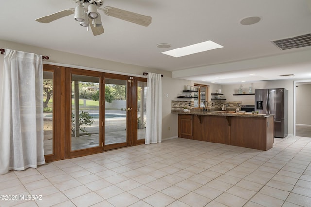kitchen with visible vents, stainless steel fridge, a peninsula, a skylight, and light tile patterned flooring