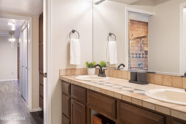 full bathroom featuring a ceiling fan, a sink, a stall shower, and wood finished floors