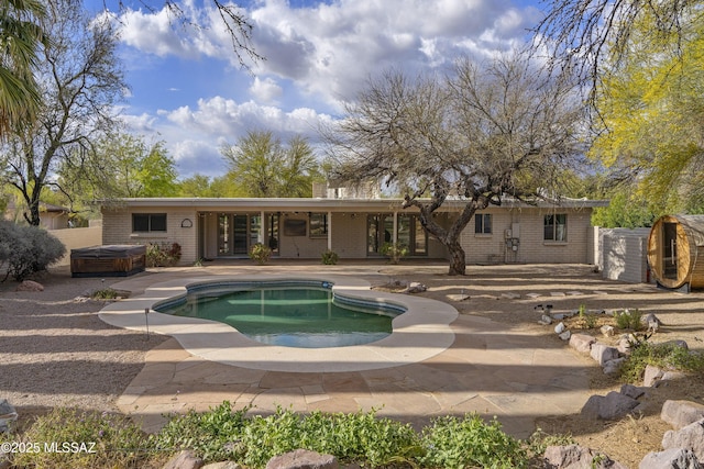 rear view of property featuring a patio, brick siding, an outdoor pool, and a hot tub