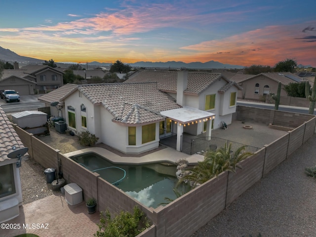 back of property at dusk featuring a fenced backyard, a tiled roof, stucco siding, a patio area, and a mountain view
