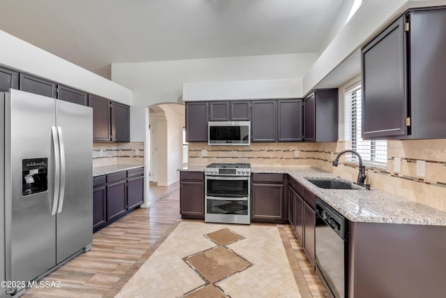 kitchen featuring sink, light stone counters, light hardwood / wood-style flooring, backsplash, and appliances with stainless steel finishes