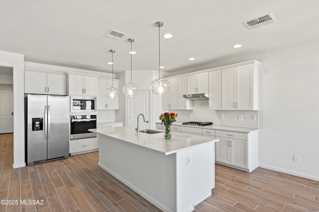 kitchen with white cabinetry, an island with sink, appliances with stainless steel finishes, decorative light fixtures, and sink