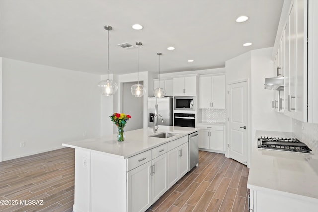 kitchen with pendant lighting, white cabinetry, stainless steel appliances, sink, and a center island with sink