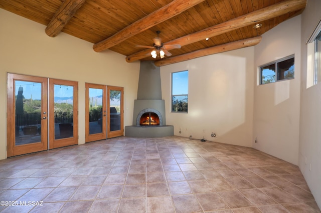 unfurnished living room with a large fireplace, wood ceiling, beamed ceiling, ceiling fan, and french doors