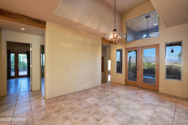 unfurnished room featuring french doors, light tile patterned floors, a towering ceiling, an inviting chandelier, and beam ceiling