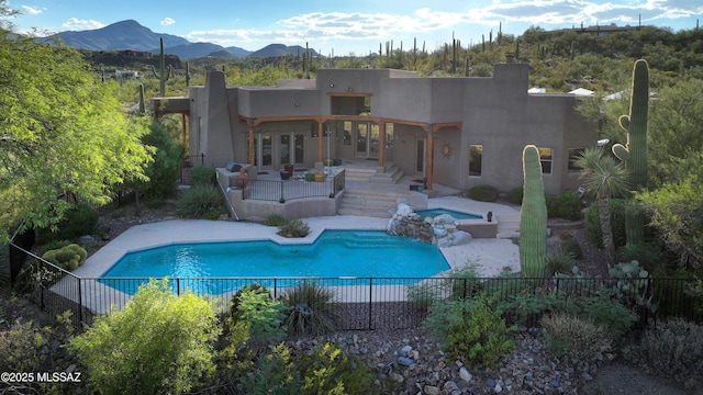 rear view of house with french doors, a patio area, a swimming pool with hot tub, and a mountain view