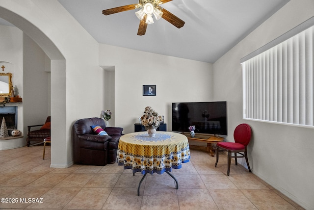 living area featuring lofted ceiling, a ceiling fan, baseboards, light tile patterned flooring, and arched walkways