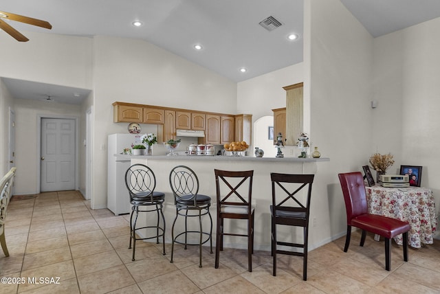 kitchen featuring freestanding refrigerator, under cabinet range hood, a breakfast bar, high vaulted ceiling, and light countertops