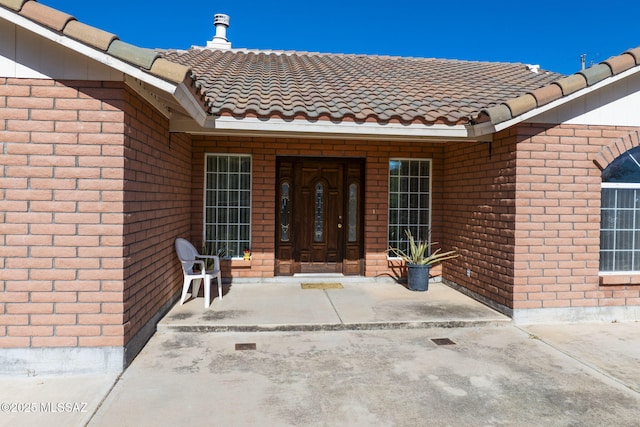 entrance to property featuring a tiled roof and brick siding